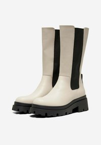 Stivali alla caviglia in pelle grigia chiara con pannelli laterali elastici neri, suola in gomma spessa e design elegante. La suola presenta scanalature di trazione pronunciate.