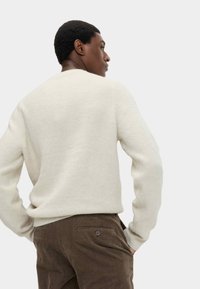 Cremfarbener, gerippter Strickpullover mit rundem Halsausschnitt, kombiniert mit braunen Cordhosen mit Seiten- und Gesäßtaschen.