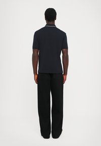 Svart polo skjorte med krage, med kortermede og slim fit. Båret med vide svarte bukser. Teksturert stoff, ensfarget.