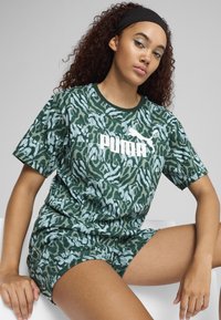 Zelené krátke rukávy tričko s vzorom a textúrovaným dizajnom, s bielym logom Puma, skombinované s nohavicami rovnakého vzoru, obe vyrobené z mäkkého materiálu.