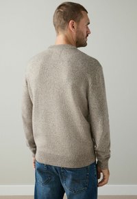 Beige striktrøje med rund hals, ribstrikkede manchetter og kant; iført med blå denim jeans, der viser et tekstureret stof og en afslappet pasform.
