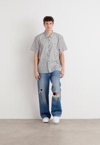 Kortermet skjorte med krage i grå og hvite vertikale striper, kombinert med lyseblå slitne jeans og hvite sneakers.