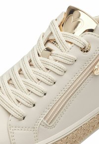 Baskets en cuir blanc avec des accents dorés, fermeture éclair texturée sur le côté et lacets crème. Dotées d'une semelle tissée beige et de détails métalliques sur la languette.
