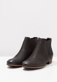 Ein Paar schwarze Leder-Stiefeletten mit niedrigen Holzabsätzen und elastischen Seitenpartien auf weißer Oberfläche.