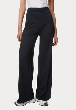 Pantalons larges bleu marine en tissu lisse. Dotés d'une taille haute et de plis à l'avant, associés à des baskets blanches.