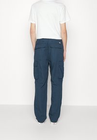 Marina cargo-byxor med flera sidofickor, lös passform, tillverkade av ett texturerat tyg, parat med en vanlig vit t-shirt.