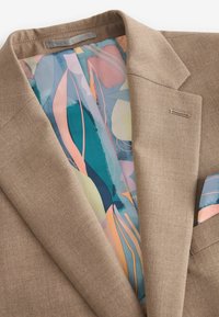 Brauner Blazer mit strukturiertem Äußeren, der ein farbenfrohes, abstraktes Futter und ein passendes Taschentuch in hellblau und rosa Tönen aufweist.
