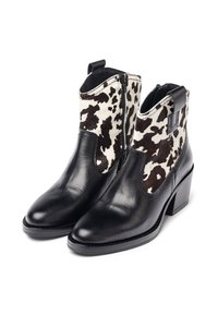Botines de cuero negro con tacones gruesos, que presentan paneles con estampado de piel de vaca en blanco y negro y cremalleras laterales.