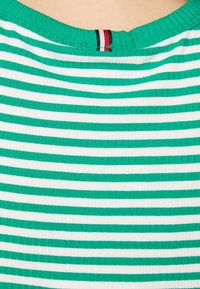 Top a rayas verdes y blancas con textura acanalada, que presenta un escote redondo y un pequeño detalle de etiqueta en rojo, blanco y azul en la costura del cuello.