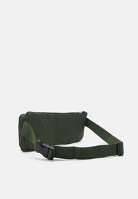 Borsa a tracolla verde in tessuto con chiusura a zip, tracolla regolabile e forma rettangolare. Presenta un'esterno liscio e un design minimalista.