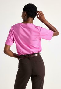 Kortærmet pink t-shirt lavet af bomuld, med en afslappet pasform. Båret med mørkebrune bukser og et brunt bælte. Minimale søm.