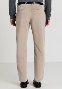 Pantaloni in corduroy beige con una finitura testurizzata, dotati di tasche posteriori e design a gamba dritta. Abbinati a scarpe nere.