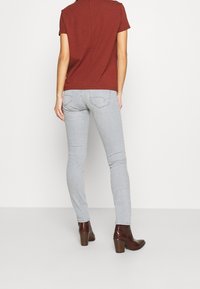 Röd kortärmad topp och ljusgrå slim-fit jeans, kombinerat med bruna klackboots. Slät tyg med en figurnära design och minimala detaljer.