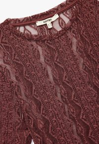 Top de encaje burdeos con escote redondo, patrón texturizado y tejido semitransparente. La etiqueta dice "Koton" con información de talla.