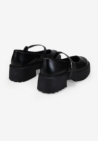 Zapatos Mary Jane negros con suela de goma gruesa, con parte superior de cuero suave y una correa delgada con una hebilla de metal.