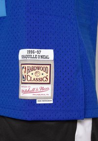 Sininen verkkopalloilupaita, jossa on valkoinen etiketti, jossa lukee "1996-97 Shaquille O'Neal" ja "Hardwood Classics" -logot alareunassa.