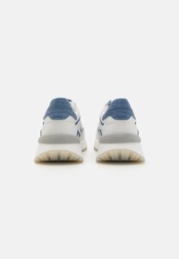 Baskets de sport blanches et bleues avec une tige texturée, des accents gris et une semelle épaisse et crantée pour un bon soutien et une stabilité accrue.