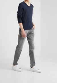 Chemise bleu marine à col en V et manches longues, tissu doux ; associée à un jean gris clair à jambes droites et des baskets blanches. Design minimaliste, sans motifs apparents.