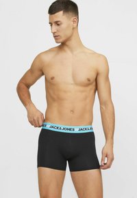 Zwarte boxershorts met een lichtblauwe elastische tailleband waarop het logo "JACK & JONES" staat. Glad materiaal, slimfit ontwerp, middellange lengte tot halverwege de dij.