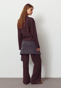 Top a maniche lunghe marrone a coste e pantaloni a gamba larga, sovrapposti a una sciarpa lavorata a maglia grigia. Tessuto morbido, vestibilità rilassata e palette di colori neutri.