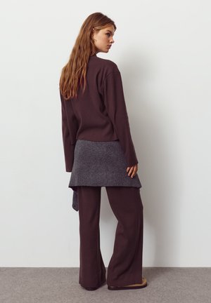 Hnedý rebrovaný top s dlhým rukávom a široké nohavice, kombinované so sivým pleteným prehozom. Mäkká textúra, voľný strih a neutrálna farebná paleta.