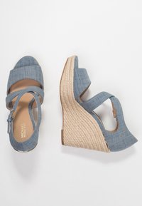 Sandały na koturnie z denimu z krzyżującymi się paskami, w jasnoniebieskim kolorze, z naturalnym, słomkowym koturnem oraz bocznym zamkiem błyskawicznym dla łatwego zakładania.