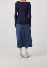 Marineblauw langemouwen top gecombineerd met een mid-length blauwe denim rok met zijzakken. Het model draagt witte sokken en sneakers.