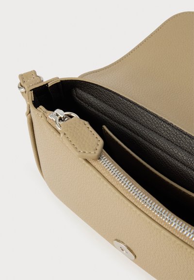 Μπεζ δερμάτινη τσάντα με υφή, που διαθέτει ασημένιο φερμουάρ και μαύρο εσωτερικό. Εμφανίζει μινιμαλιστικό, γωνιακό σχεδιασμό.