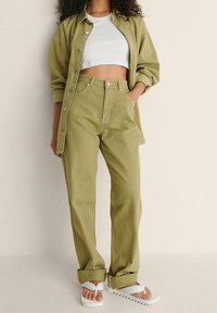 Olivgrüne, hochtaillierte Hosen mit lässiger Passform und umgeschlagenen Säumen, kombiniert mit einem weißen Croptop und weißen Sandalen. Weicher, strukturierter Stoff.