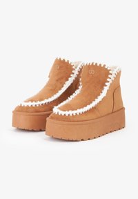 Stivaletti alla caviglia in suede color cammello con fodera bianca pelosa e bordo a scallop. La suola spessa e testurizzata offre maggiore altezza e stabilità.