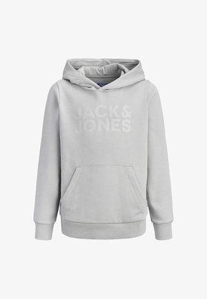 Noor inimene seisab, kandes heledat halli kapuutsiga pusa, musti teksaseid, must-valgeid tossusid ja musta mütsi "Jack & Jones" logoga.