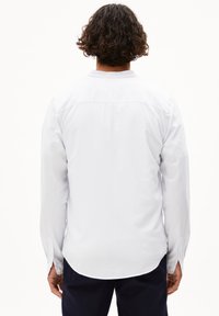 Weißes Langarmshirt mit geradem Saum, knöpfbaren Manschetten und Schulterpasse, aus glattem Stoff, von hinten gezeigt.