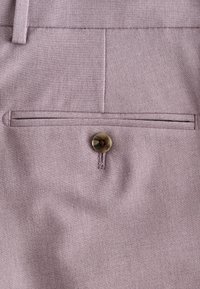 Jasnofioletowy materiał o gładkiej fakturze, z przeszytą kieszenią i brązowym guzikiem jako detalem. Prosty wzór bez widocznych zdobień.