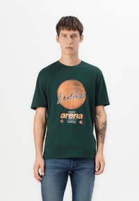 Mørkegrøn bomuld t-shirt med et basketballgrafik og tekst i orange. Designet inkluderer korte ærmer og rund hals.