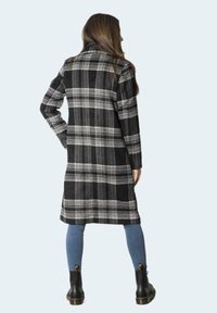 Černobílý kostkovaný kabát s dlouhým střihem, s klopovým límcem a bočními kapsami. Nosit s modrými džíny a černými šněrovacími botami.