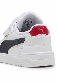 Hvide sneakers med sort side-stribe, rød hæl-accents og tekstureret detaljer. Har velcro-stropper og præget "Puma" logo på hælen.