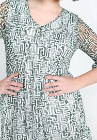 Robe verte et blanche à motifs avec un décolleté en V, dotée de manches semi-transparentes. Le design comprend des formes géométriques et des lignes.