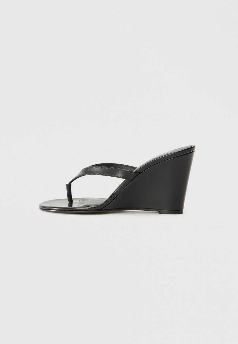 Sandales à talons compensés noires avec un dessus en cuir lisse, comprenant deux fines lanières et un bout rond. Le talon compensé est solide et légèrement surélevé.