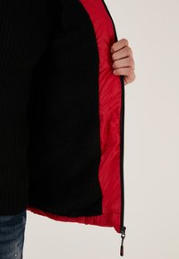 Sort jakke med rød foring, der har en blød fleece indvendig og en glat yderside. Lynlås lukning foran med holdbare metaldele.