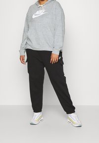 Grå Nike-huvtröja med logotyp fram, kombinerad med svarta cargo-byxor med sidofickor. Modellen bär ljusa sneakers med mönstrad design.