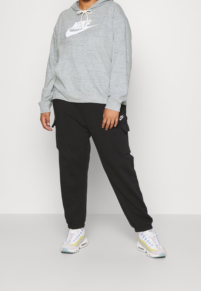 Grå Nike-huvtröja med logotyp fram, kombinerad med svarta cargo-byxor med sidofickor. Modellen bär ljusa sneakers med mönstrad design.