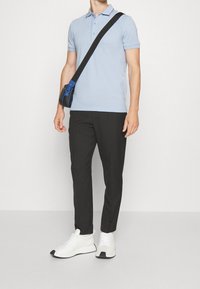Světle modré polo tričko s límečkem a krátkými rukávy, v kombinaci s černými kalhotami a bílými teniskami s černým akcentem. Malá crossbody taška.