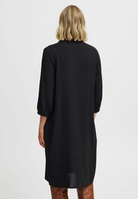 Fekete midi ruha texturált anyagból, háromnegyedes ujjakkal és laza szabással. Az alja hátul egy kicsit hosszabb.