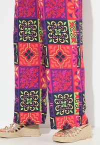Kleurrijke, gestreepte wijde broek met levendige vierkanten van bloem- en geometrische ontwerpen in rood, roze, paars en groen. In combinatie met sleehakken.