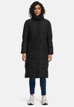Black padded coat with high collar, front buttons, drawstring waist, and two pockets. Styled with slim jeans and sneakers.