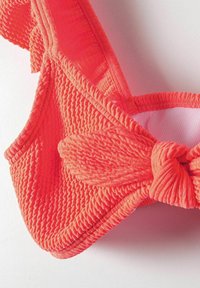 Kostium bikini w kolorze koralowym z teksturą, z falbaniastymi brzegami i węzłem na środku. Gładkie wewnętrzne wykończenie. Regulowane ramiączka w tym samym kolorze.