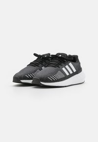 Scarpe da ginnastica nere e grigie con una tomaia testurizzata, accento bianco a tre strisce sul lato e una suola bianca a contrasto. Design con i lacci.