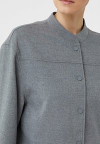 Szara teksturowana kurtka z kołnierzem typu mandarynka, z zapięciem na guziki z przodu i subtelnym przeszyciem na ramionach.