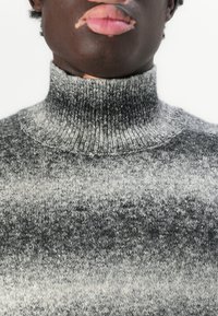 Pull en maille gris à col roulé avec un motif en dégradé, passant d'un gris foncé à un gris clair, et une texture de col côtelé.