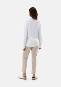 Camicia bianca a maniche lunghe con colletto, abbinata a pantaloni beige e scarpe con dettagli neri. Tessuto liscio e design su misura.